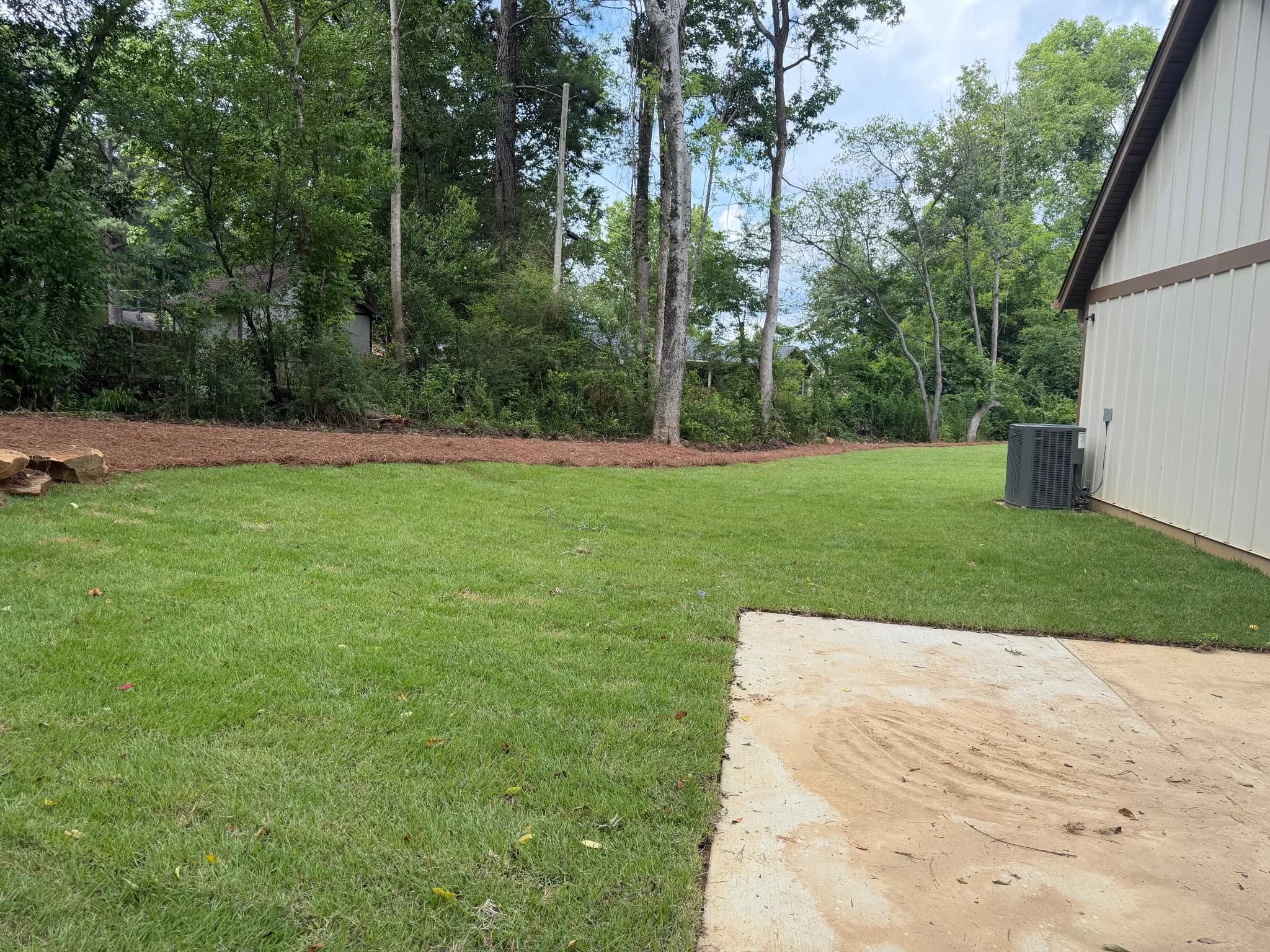 Cleared yard with freshly laid grass and a building in the foreground.