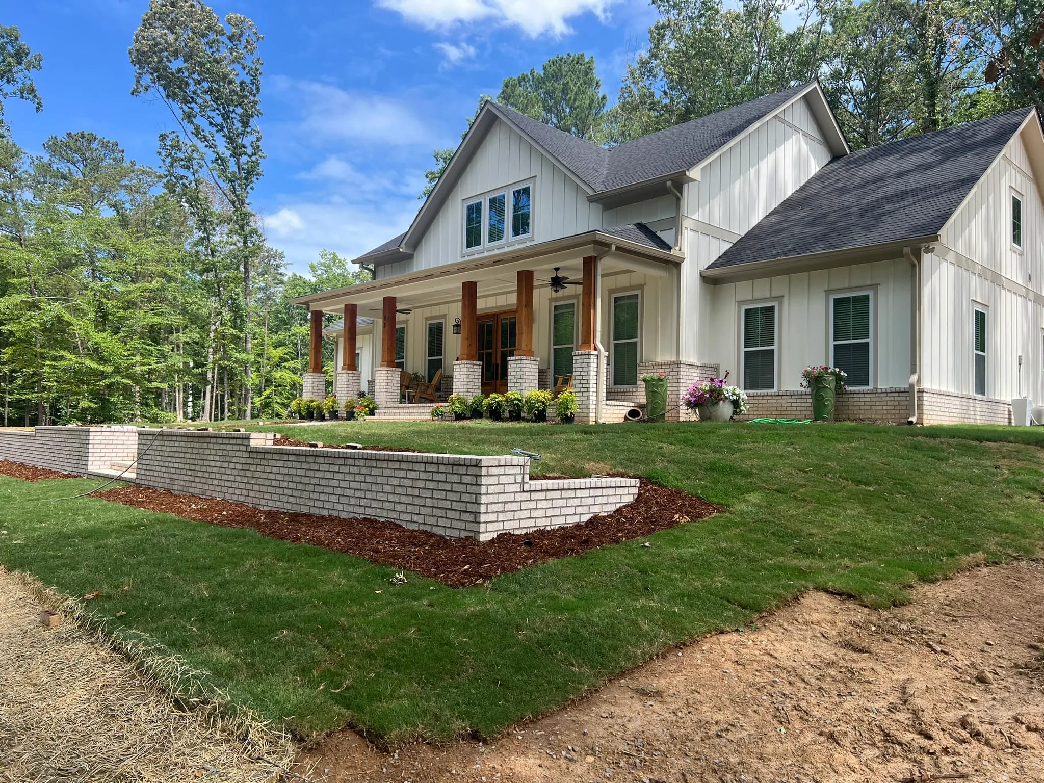This project showcases the finished landscaping around a newly built home, featuring stone retaining walls and lush garden beds.